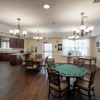 A cozy dining area with a poker table and a view into the kitchen, featuring elegant chandeliers and hardwood flooring.