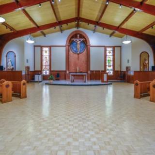 The interior of a church with an altar, rows of pews, and stained glass windows.