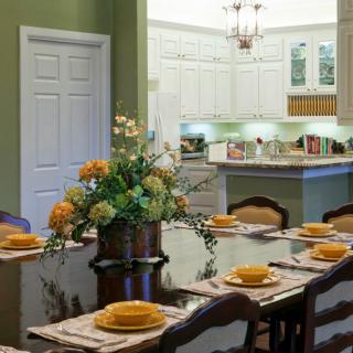 A beautifully arranged dining table set for a meal, with a floral centerpiece and adjacent view of a kitchen.