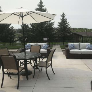 A patio featuring outdoor furniture, including a table with chairs and an umbrella, set against a backdrop of trees.
