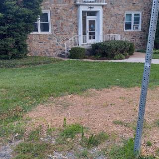 A view of a stone building with landscaped grass and a signpost nearby.