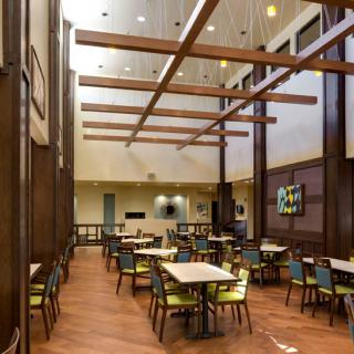 A modern dining area with wooden beams, tables, and vibrant chairs.