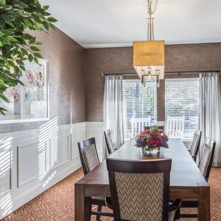 A beautifully furnished dining room with a large table, surrounded by chairs, and illuminated by natural light through large windows.