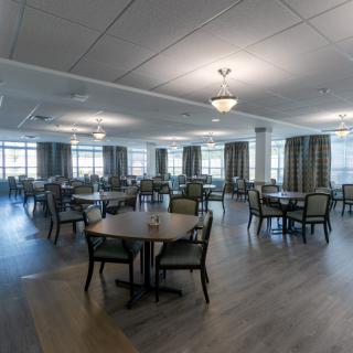 A spacious and modern dining area with multiple tables and chairs, well-lit with ceiling lights.