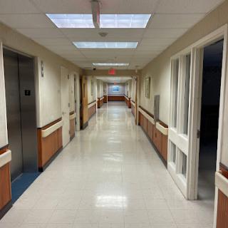 A long, well-lit hospital hallway with doors on the sides and an elevator in the background.