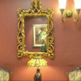 Elegant interior decor featuring a gilded mirror, a decorative lamp, and framed artwork.