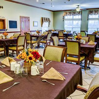 A neatly arranged dining room with tables set for a meal, featuring floral centerpieces.
