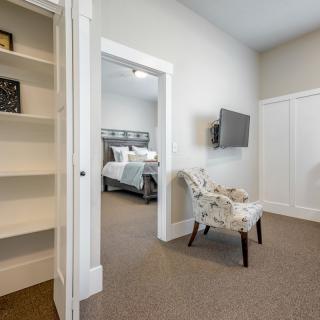 A modern bedroom with a cozy setup featuring a large bed, a mounted television, an elegant chair, and built-in shelves.