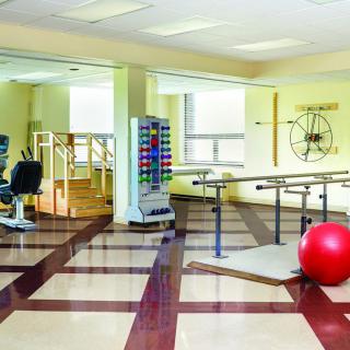 A well-equipped physical therapy room with various rehabilitation tools and exercise equipment, including parallel bars and a large red therapy ball.