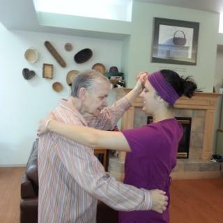An elderly man and a woman are engaged in a dance, sharing a joyful moment indoors.