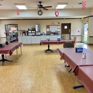 An empty community center room with decorated tables and a kitchen area in the background.