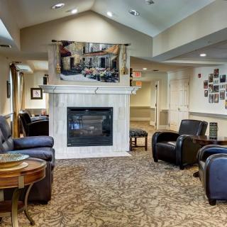 A cozy living room with armchairs and a fireplace, featuring warm lighting and carpeted flooring.