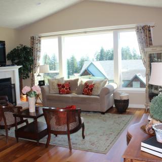 A cozy living room with a sofa and chairs arranged around a coffee table, featuring a fireplace and large window with scenic views.