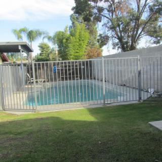 A fenced swimming pool in a spacious backyard surrounded by trees.