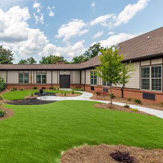 A pleasant view of a landscaped garden with a modern building in the background, featuring a well-maintained lawn and clear skies.
