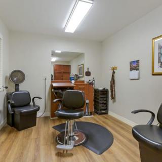 An empty barbershop with chairs and a mirror, featuring a wooden floor and bright lighting.