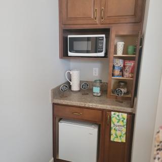 A compact kitchenette with a microwave, mini fridge, coffee maker, and shelves stocked with various items.