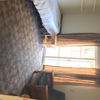 A cozy bedroom with a bed, carpeted floor, and large window allowing natural light.