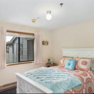A cozy bedroom with a neatly made bed, colorful bedding, and a large window offering natural light.