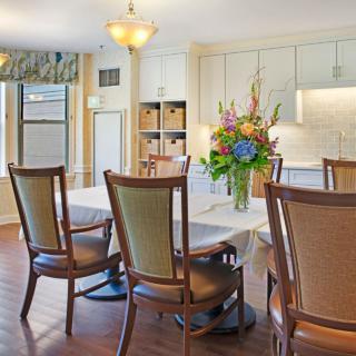 A modern dining area with a table and chairs, featuring a vase of flowers and ample natural light.