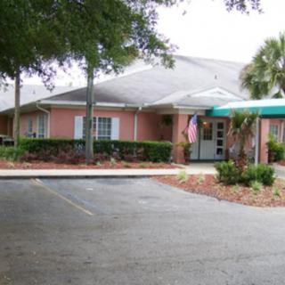 A small, single-story building with a driveway and palm trees in front.