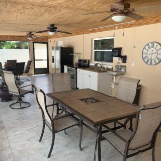 A spacious outdoor patio featuring a dining table, kitchenette, and ceiling fans.