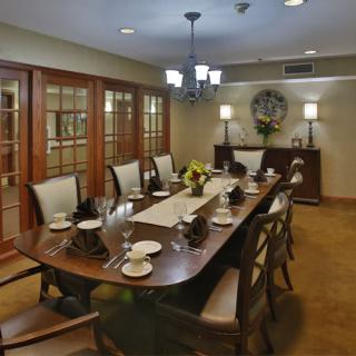 An elegantly set dining room with a large wooden table and comfortable chairs, featuring sophisticated decor and soft lighting.