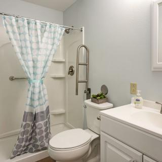 A well-lit bathroom featuring a shower with a patterned curtain, a toilet, and a sink with a mirror above.