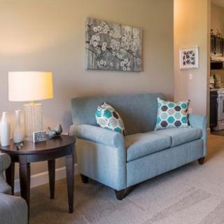 A cozy living room with a blue sofa, decorative cushions, a side table with a lamp, and artwork on the wall.