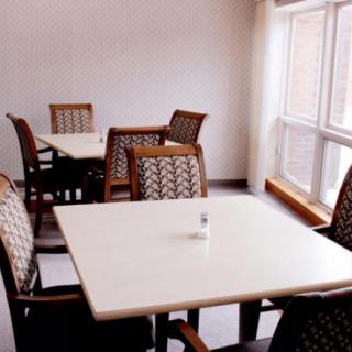 A quiet dining area with several tables and chairs, illuminated by natural light from a large window.