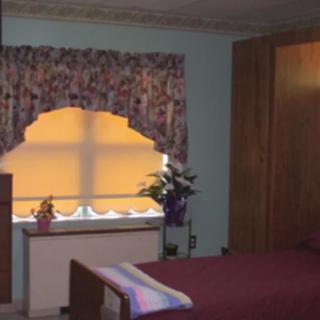A cozy bedroom with a decorative window and curtains, featuring a bed and wooden furniture.