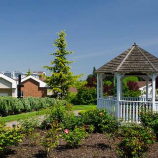 A picturesque garden with a white gazebo and houses in the background under a clear blue sky.