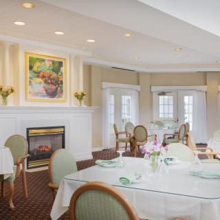 A beautifully decorated dining room with round tables, elegant chairs, and a cozy fireplace.