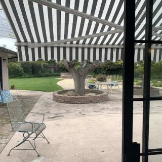 A cozy outdoor patio view featuring a tree and lawn area, shaded by a striped awning.