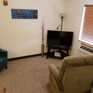 A cozy living room with a television, armchair, and window blinds.