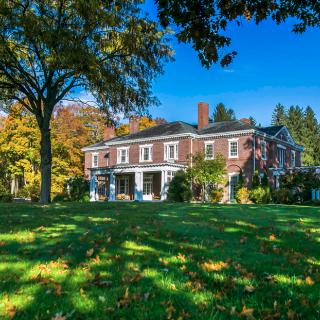 A beautiful brick mansion surrounded by trees in an autumn setting.