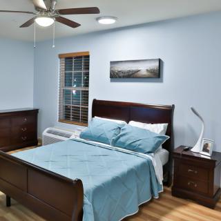 A cozy bedroom featuring a bed with blue bedding, wooden furniture, and a ceiling fan.