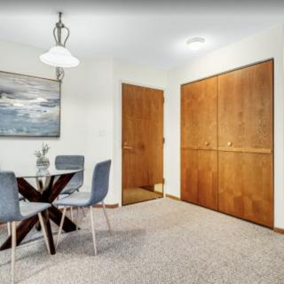 A modern dining area featuring a round table with four chairs, a large painting on the wall, and wooden closet doors.