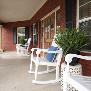 A cozy porch featuring white rocking chairs and lush plants, perfect for relaxation.