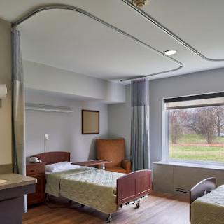 A well-lit hospital patient room featuring two beds, a chair, and a view outside the window.