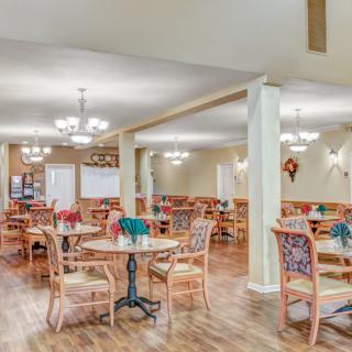 A spacious dining area with neatly arranged tables and chairs, illuminated by elegant chandeliers.