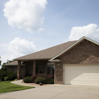 A modern brick house with a garage and well-maintained landscaping under a cloudy sky.