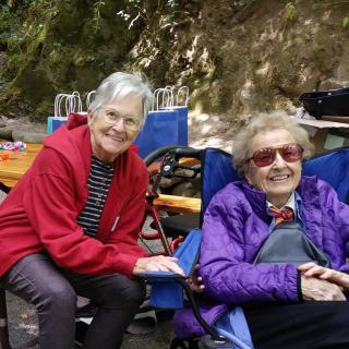 Two elderly women enjoying a sunny day outdoors, sitting comfortably in chairs.
