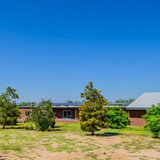 A rural house surrounded by trees under a clear blue sky.