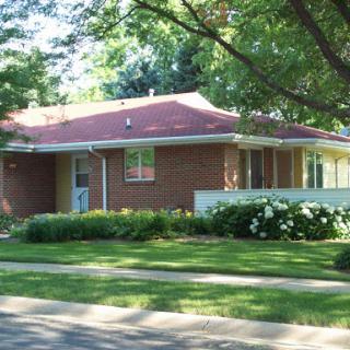 A charming brick house surrounded by lush greenery in a suburban neighborhood.