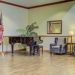 A room with a grand piano, American flag, armchair, lamp, mirror, and plant.