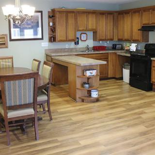 A modern kitchen and dining area featuring wooden cabinets, a hardwood floor, and a chandelier above the table.