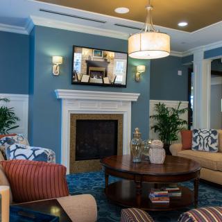 A cozy modern living room with blue walls, featuring a fireplace and a mounted television above it, surrounded by comfortable sofas and a central coffee table.