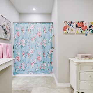A well-decorated bathroom featuring a floral shower curtain, neatly arranged towels, and artwork on the walls.