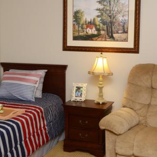 A cozy bedroom with a bed, nightstand, lamp, and recliner.